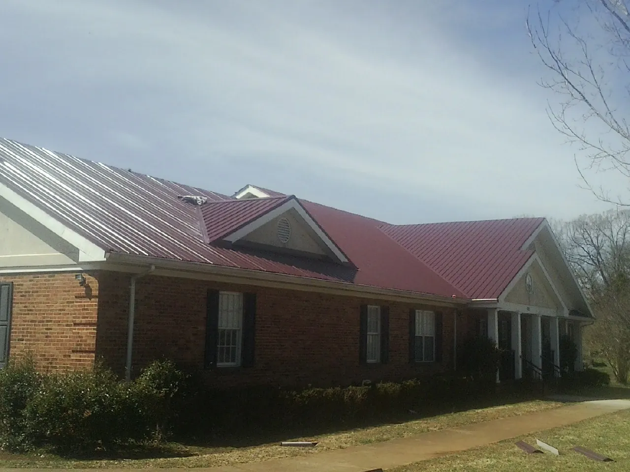 Red metal roof with gabled entries on a long brick building, from a Hail Damage Roof Repair job in West Park