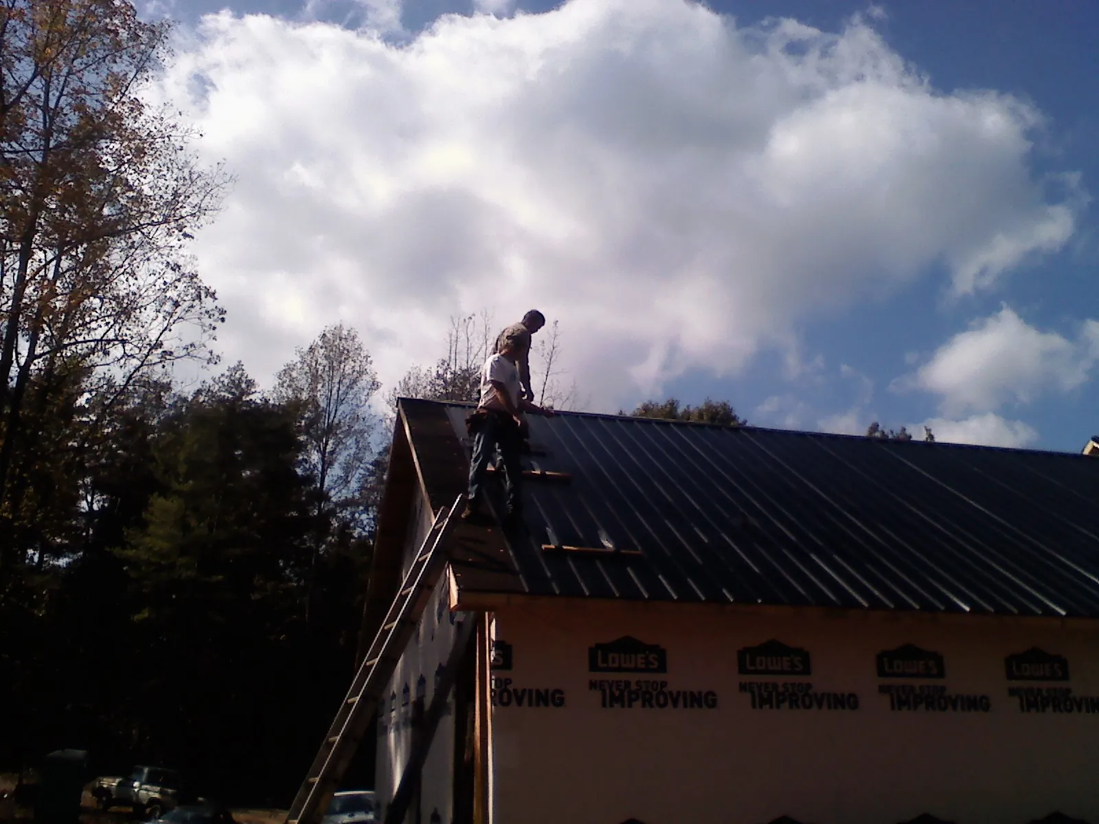 Roofer fastening dark metal panels high against a cloudy sky, from a Roof Inspection job in West Park