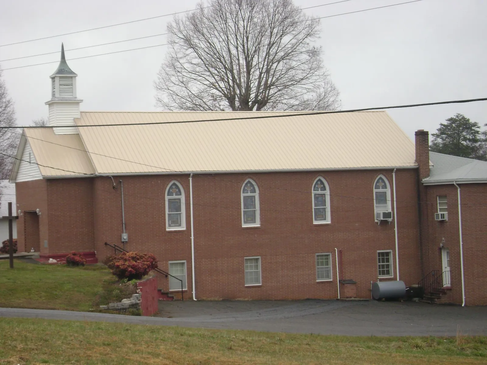 New tan metal roof on a brick church with a white steeple in West Park