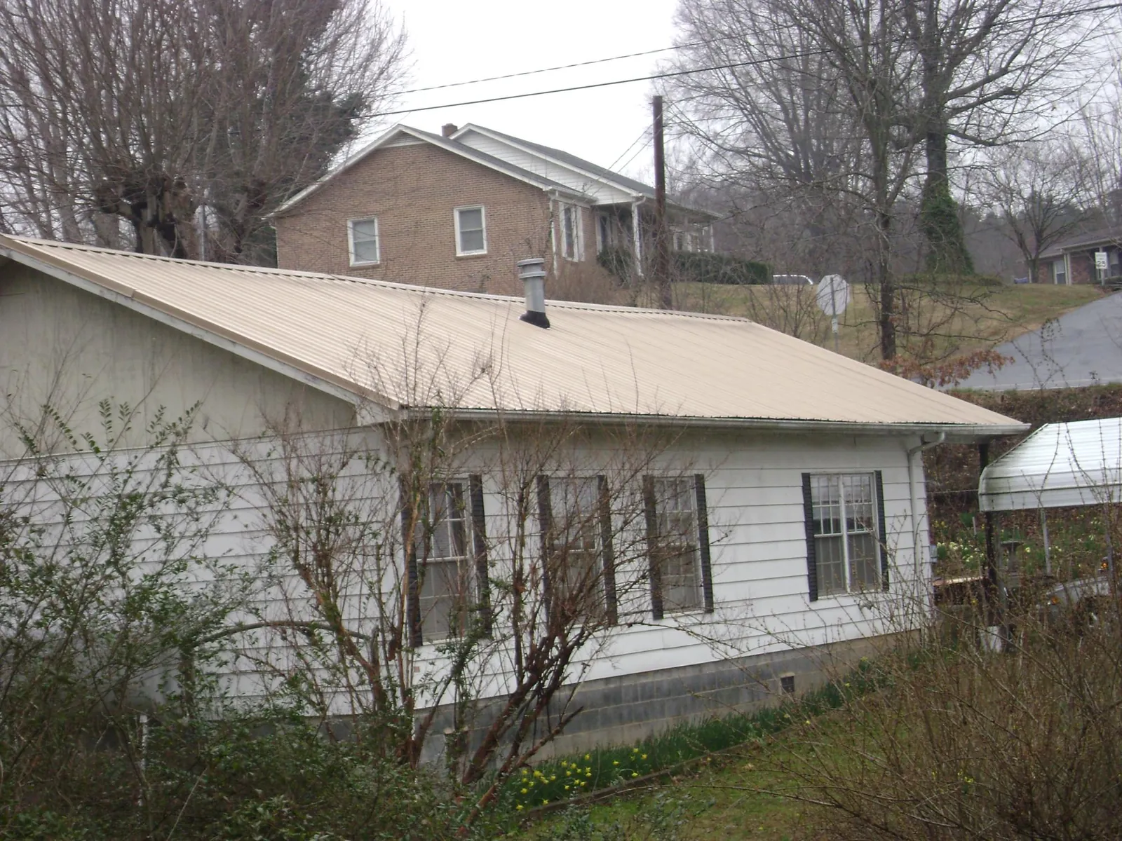 Tan metal roof on a white sided house set into a hillside — Commercial Roofing by Roofing Brothers in West Park